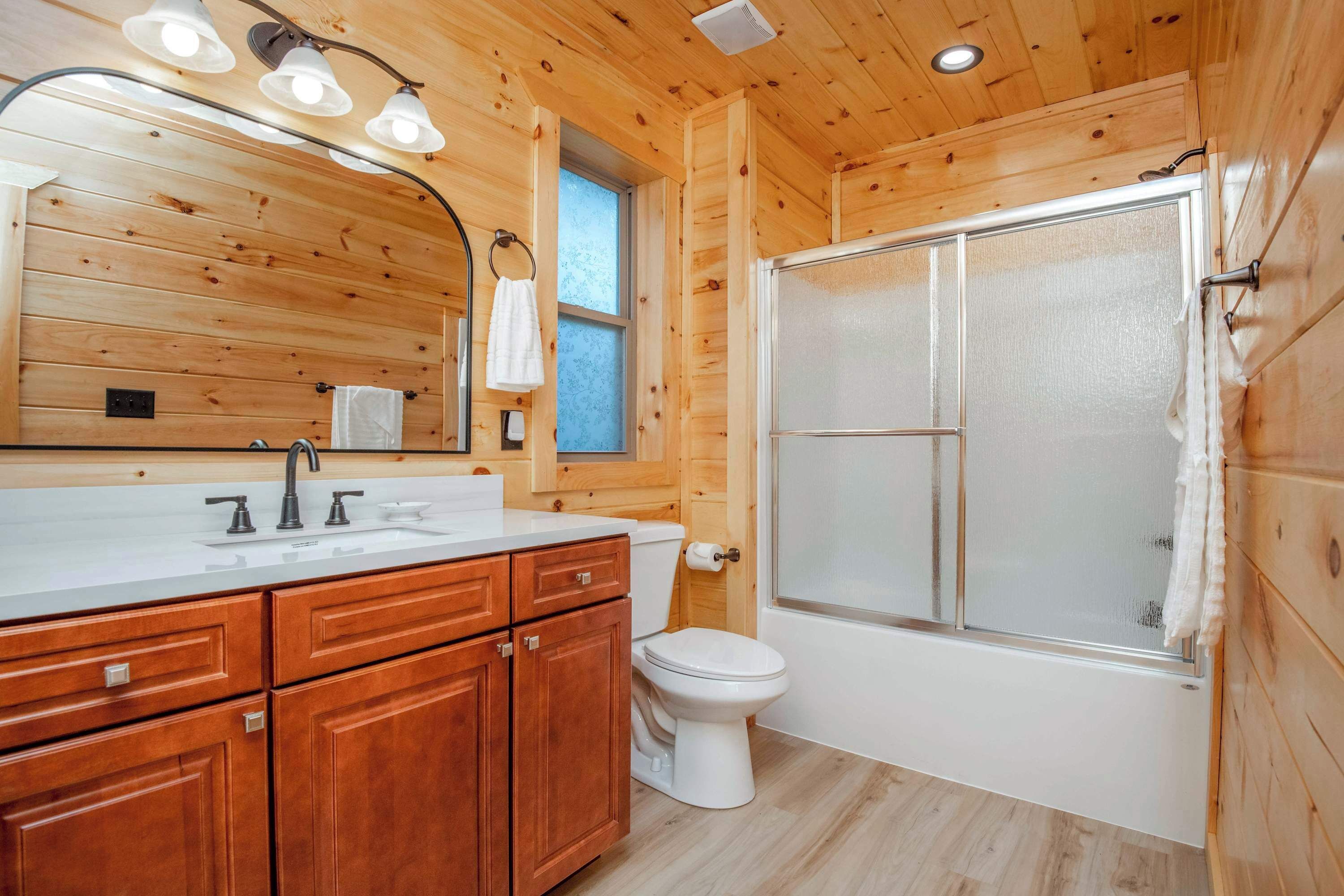 A wooden cabin bathroom with a white sink, wooden cabinets, a toilet, and a glass-enclosed shower.
