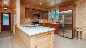 Cocina de cabaña de madera con encimera de granito, electrodomésticos de acero inoxidable y armarios de madera.