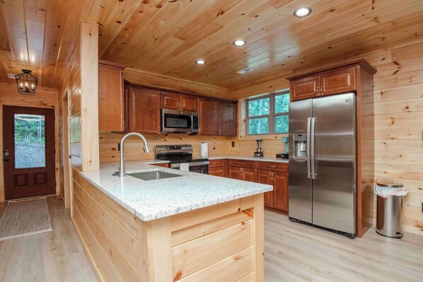 Cocina de cabaña de madera con encimera de granito, electrodomésticos de acero inoxidable y armarios de madera.
