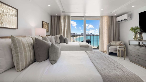 Un dormitorio moderno con una cama grande, un sofá, un televisor y vistas al mar.