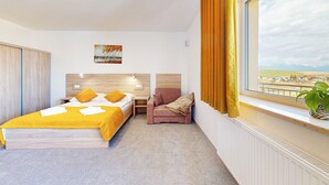Ein Hotelzimmer mit Bett, Sessel, Nachttisch, Fenster mit Vorhängen und Blick auf die Stadt.