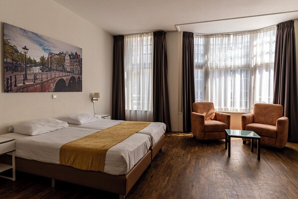 A hotel room with a large bed, two armchairs, a small table, and a painting of a bridge on the wall. - Hotel Residence Le Coin (Amsterdam)