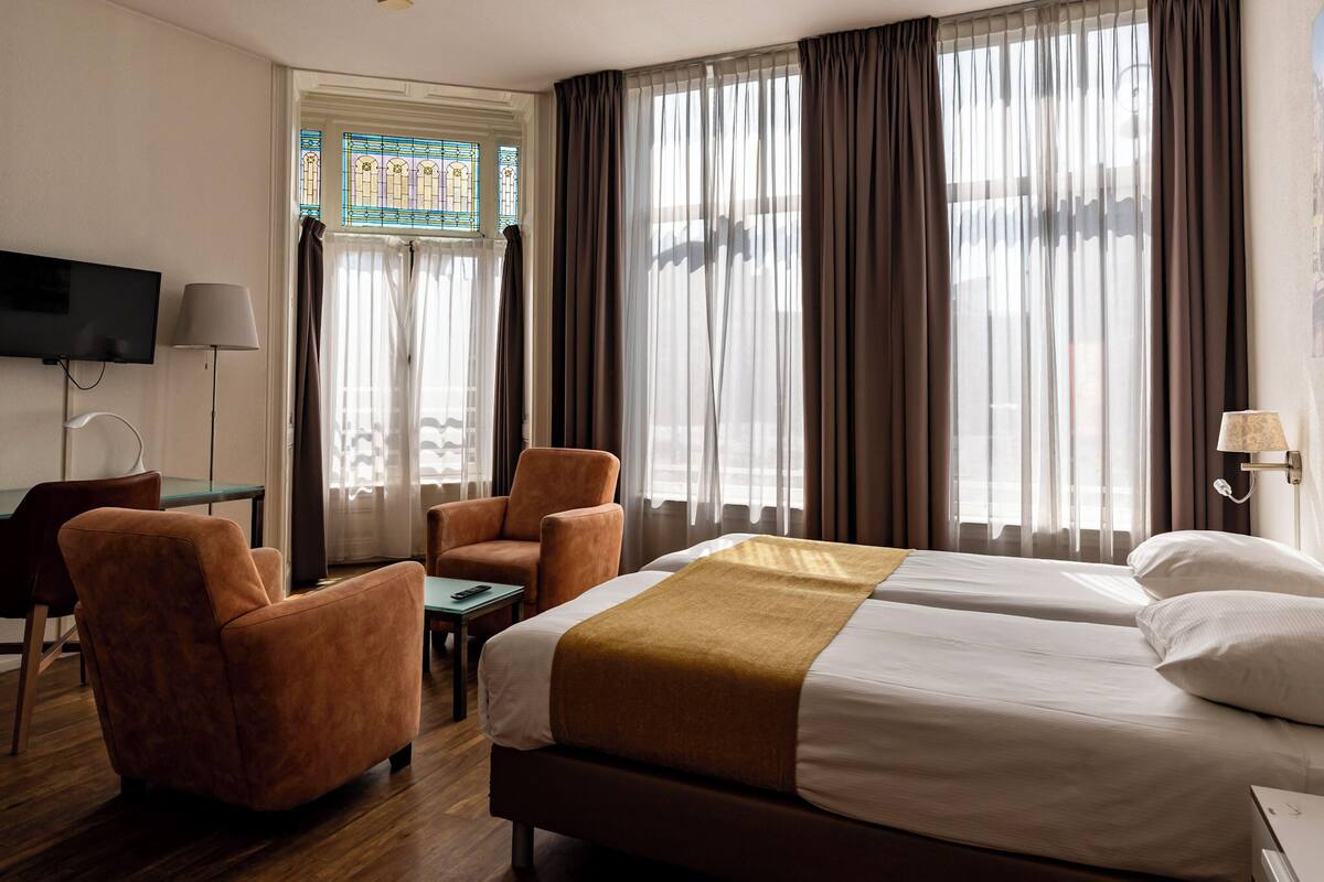 Habitación de hotel con una cama, dos sillones, una mesita, un televisor y una ventana con cortinas.
