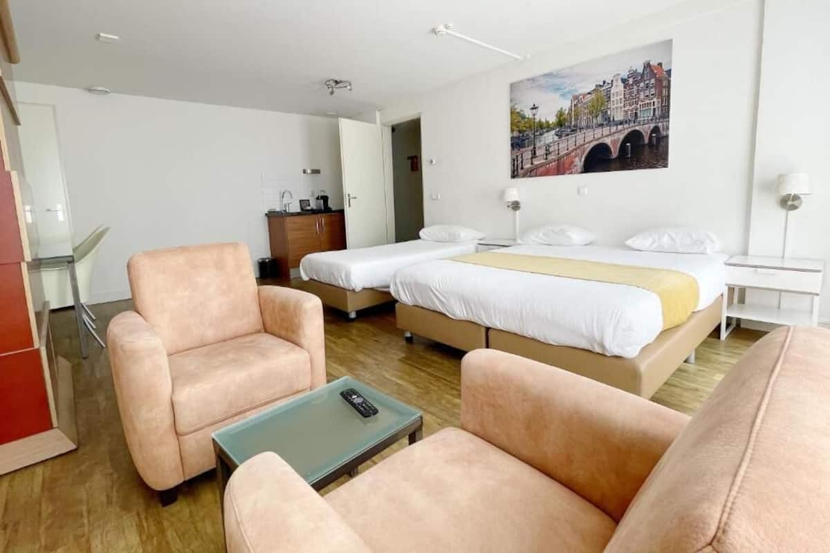 Habitación de hotel con dos camas, un sofá, una mesa de centro y un cuadro de un paisaje urbano.