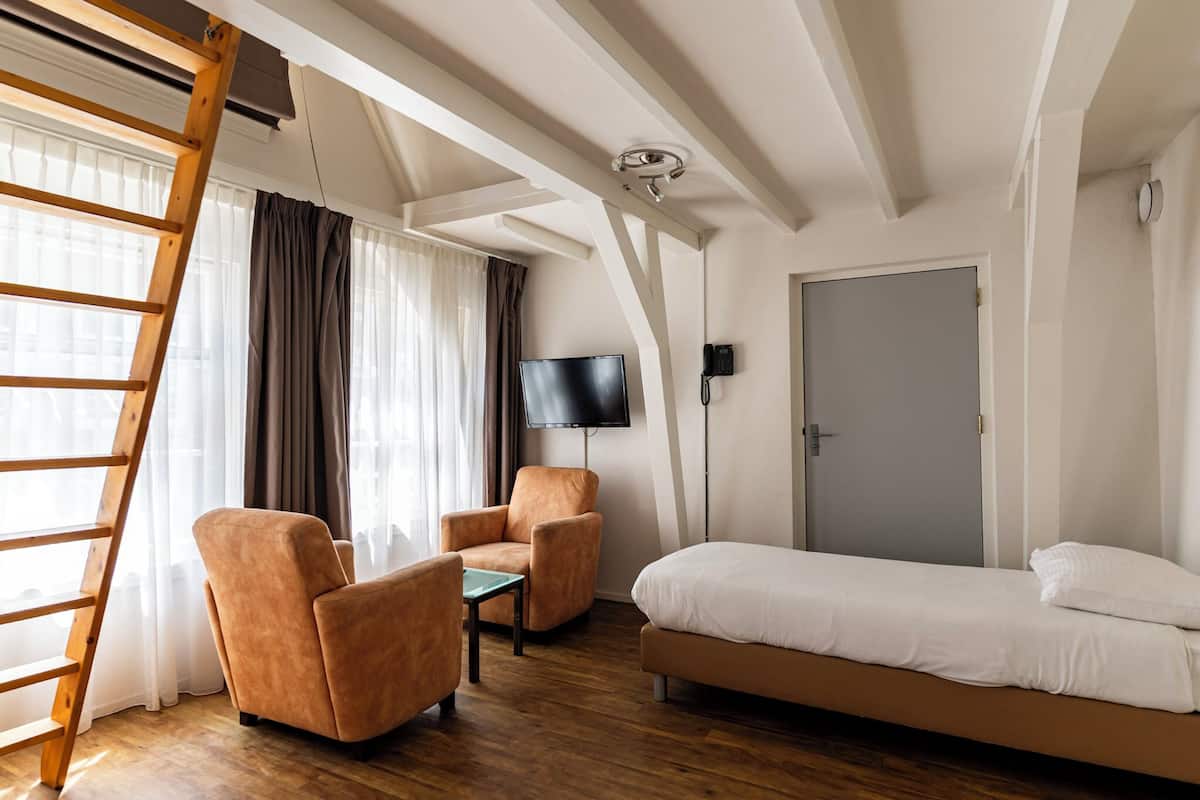 Una habitación con una cama, dos sillones, una mesita, un televisor y una puerta.