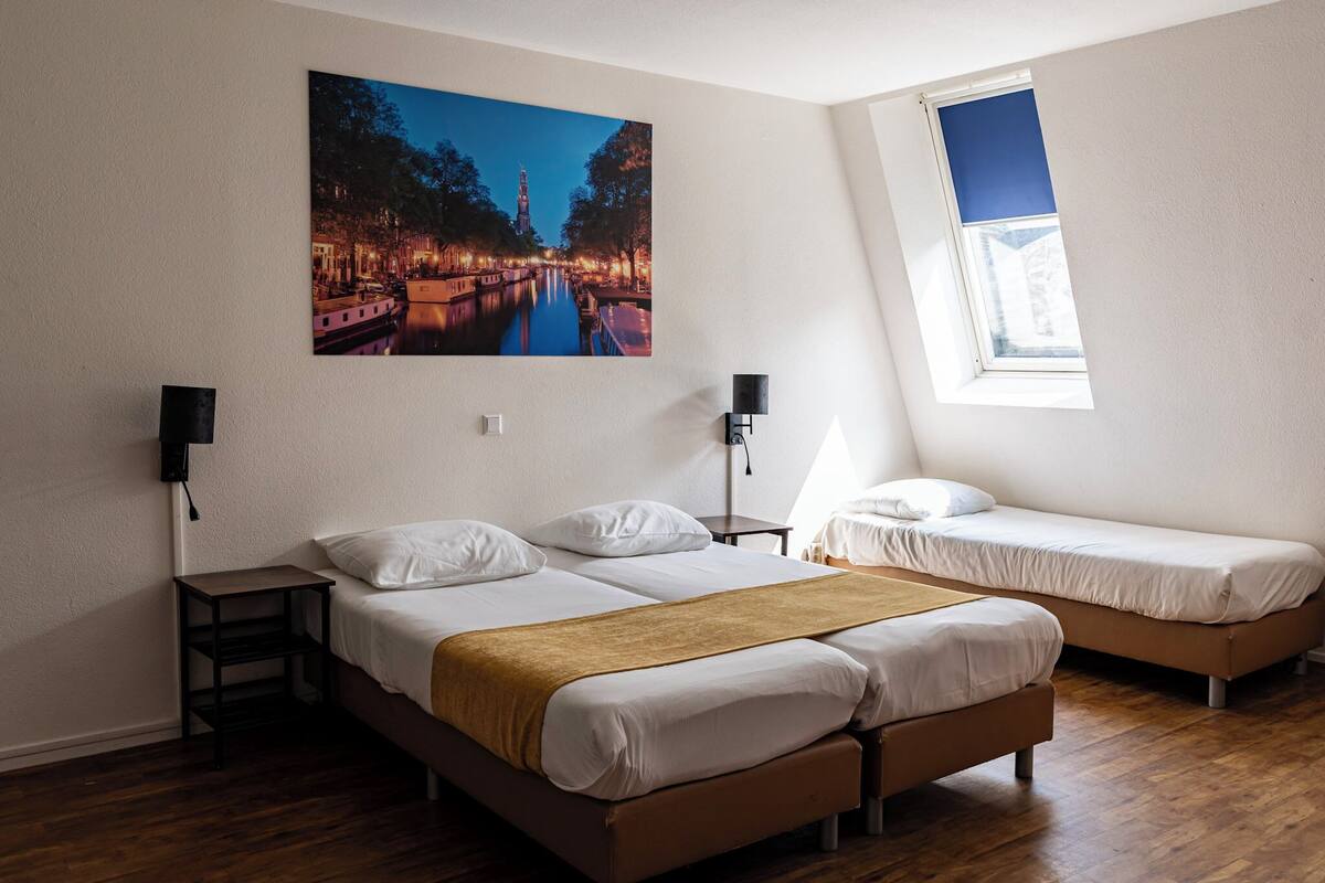 Un dormitorio con dos camas, una mesita de noche, una lámpara y una ventana.