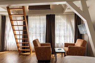 A room with a wooden ladder, two brown armchairs, a small table, and a bed.