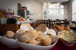 A variety of breads and pastries on a table in a dining area with a kitchen in the background.