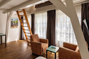 Una sala de estar moderna con una escalera de madera, un sillón marrón, una mesita y un cuadro de un paisaje urbano en la pared.