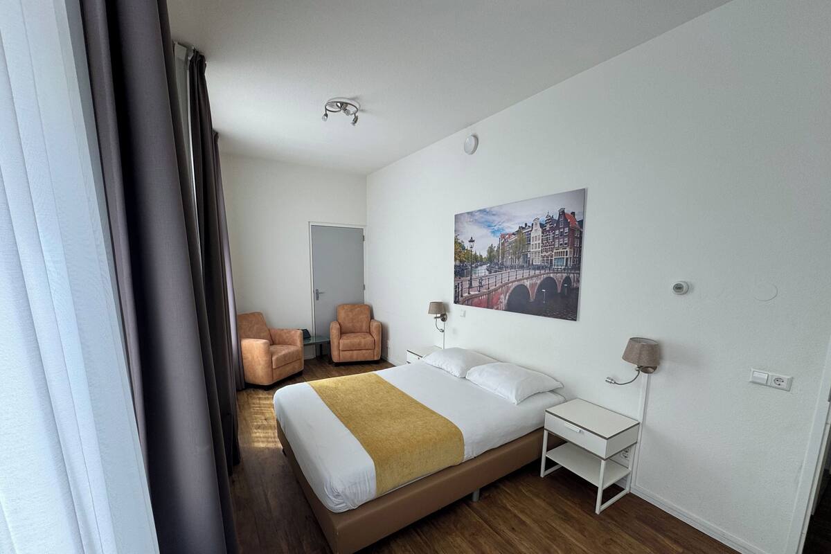 Una habitación de hotel con una cama, dos sillones, una mesita de noche y un cuadro de un puente.
