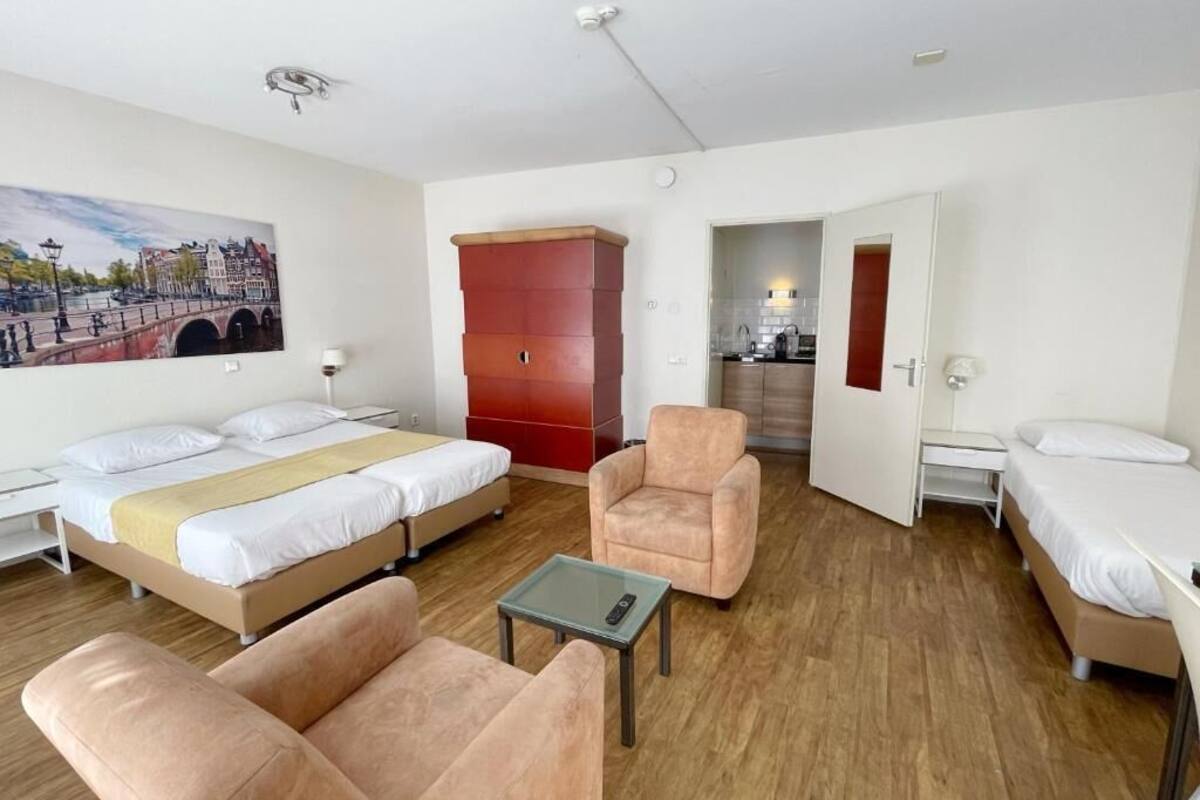 Habitación de hotel con dos camas, un sofá, una mesita y un armario rojo, además de un cuadro de un puente.