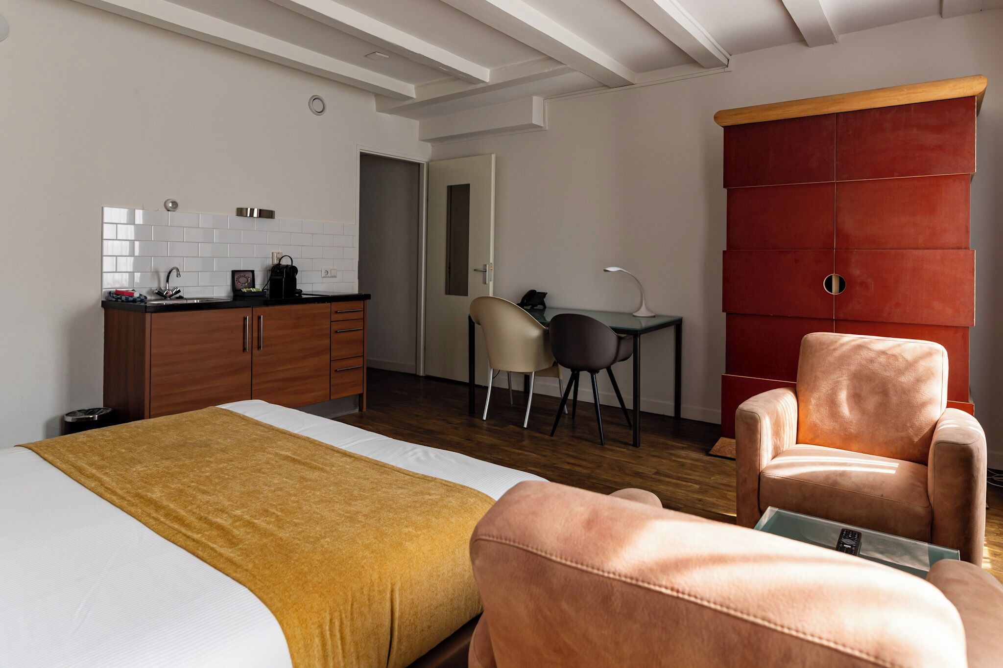 A modern hotel room with a bed, a desk, a chair, and a wardrobe.