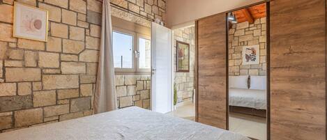 A bedroom with a stone wall, a bed with a patterned bedspread, a wooden ceiling, and a large mirror.