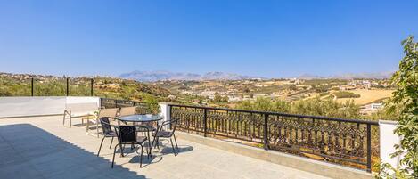 Une terrasse avec une table et des chaises, un pot de fleurs et une vue sur une vallée et des montagnes.