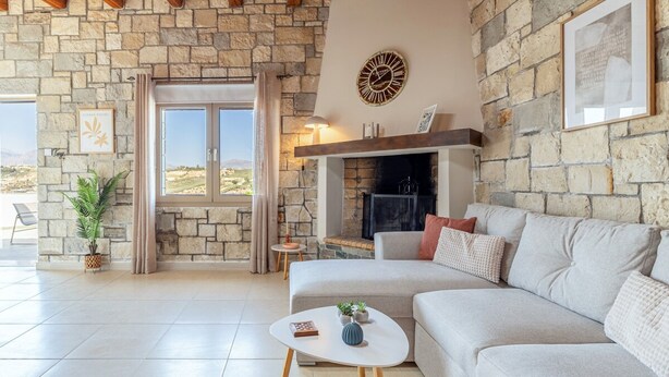 Amplia sala de estar con pared de piedra, chimenea, sofá y vistas al exterior.