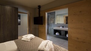 A modern hotel room with a large bed, two towels, a wooden wardrobe, a television, and a glass shower enclosure. - Luxurious Penthouse on the Golf Course (Westendorf)