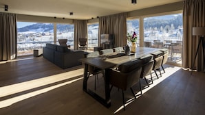 A spacious living room with a large dining table, comfortable seating, and a scenic mountain view through large windows. - Luxurious Penthouse on the Golf Course (Westendorf)