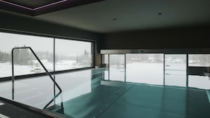 A modern indoor swimming pool with a glass wall, a metal ladder, and a view of a snowy landscape. - Luxurious Penthouse on the Golf Course (Westendorf)