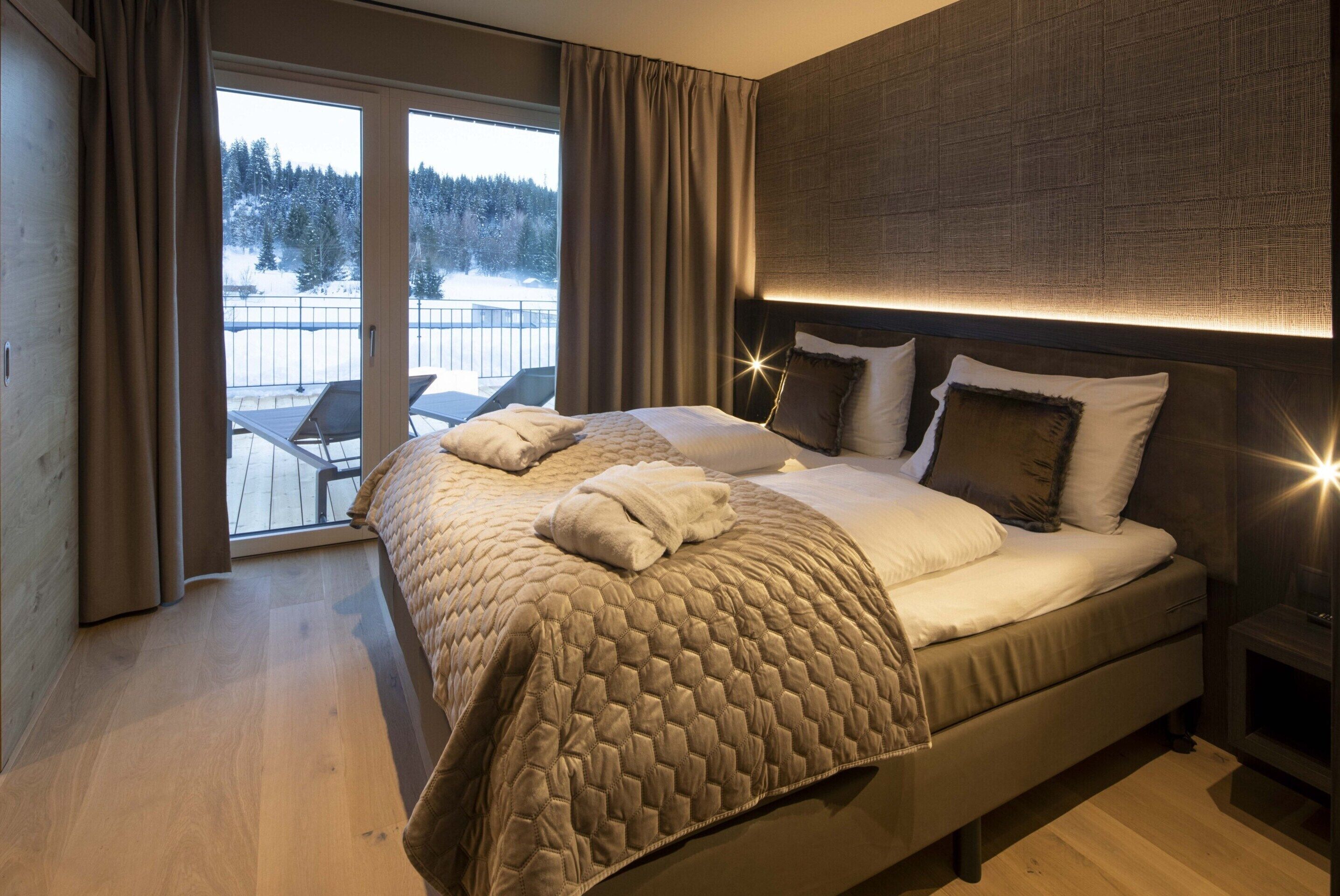 Una camera da letto moderna con un letto grande, un balcone vista su un paesaggio innevato e un camino.