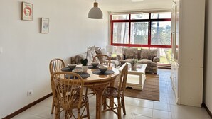 Een eethoek met een ronde tafel en stoelen, een zithoek en een groot raam met uitzicht op palmbomen.