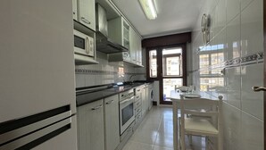 A kitchen with white cabinets, a black countertop, a microwave, an oven, and a sink. There is a window with a view of buildings outside. - Apartment in the center El Refugio 3016 (Santoña)