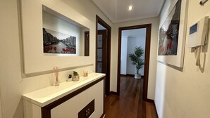 A hallway with a white console table, framed pictures on the walls, and a wooden floor. - Apartment in the center El Refugio 3016 (Santoña)