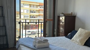 A hotel room with a bed, a wooden dresser, and a view of a building through a large window. - Apartment in the center El Refugio 3016 (Santoña)