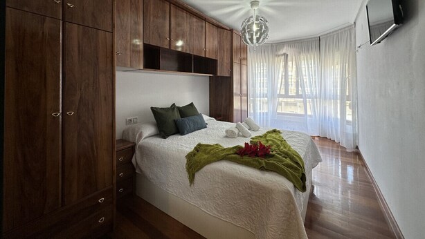 A bedroom with a large bed, wooden wardrobe, and a TV on the wall. - Apartment in the center El Refugio 3016 (Santoña)