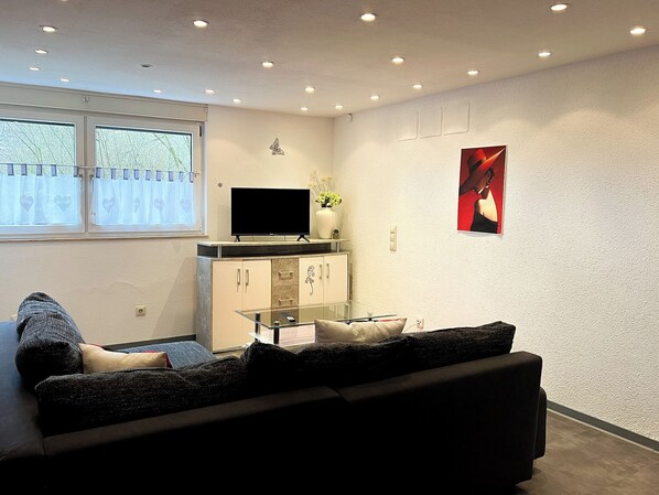 A living room with a sofa, a TV on a cabinet, a window with curtains, and a wall with a picture.