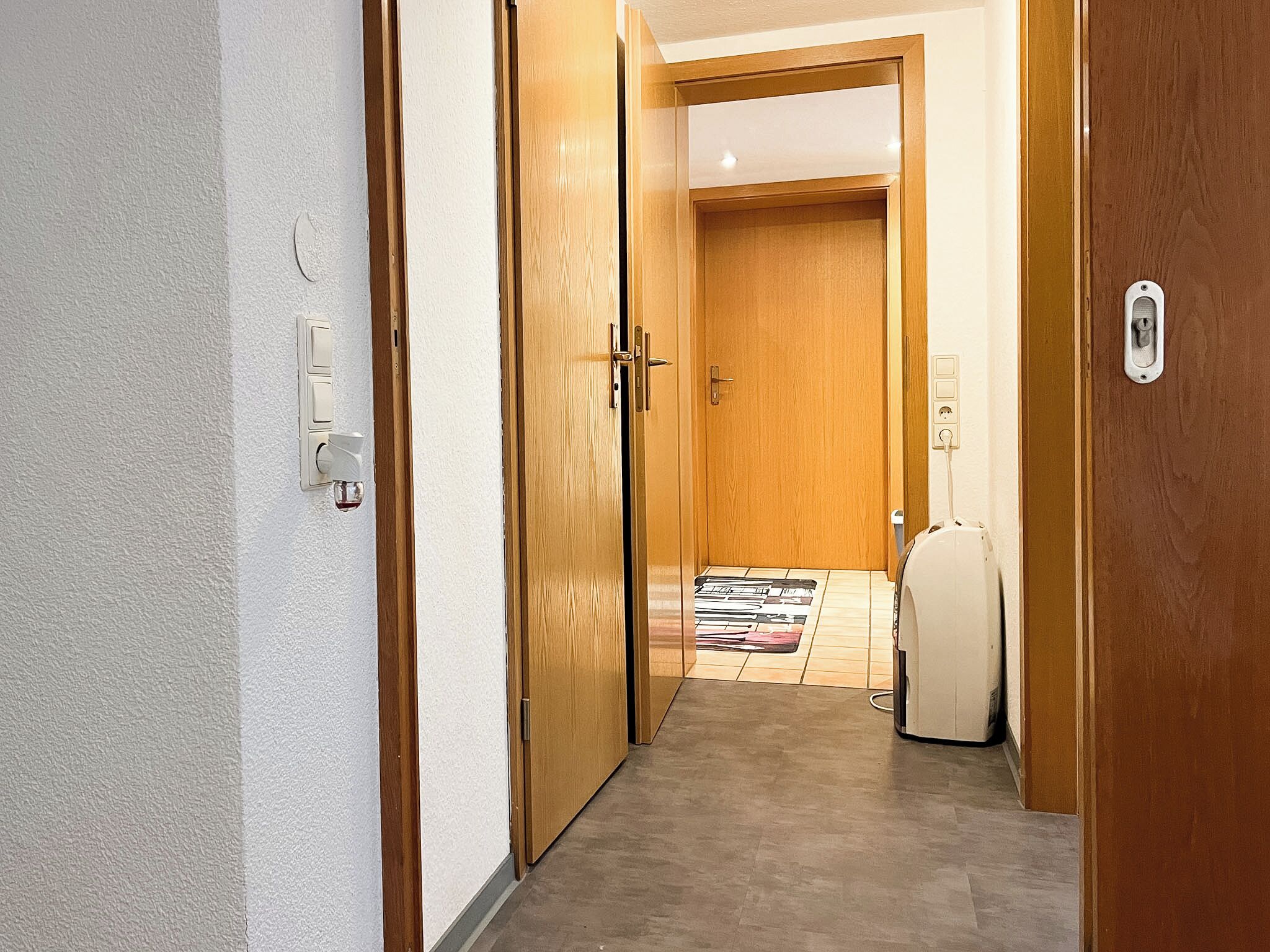 A hallway with wooden doors, a white wall, and a tiled floor.