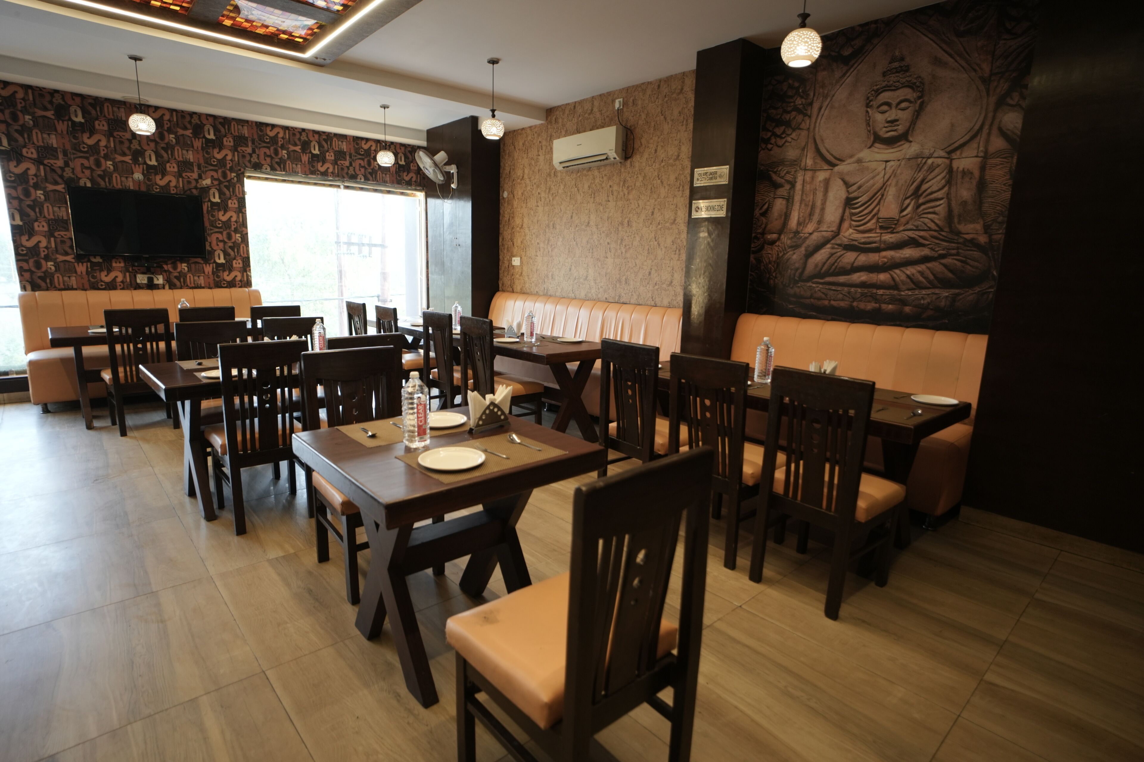 A restaurant with wooden tables and chairs, a Buddha statue on the wall, and a flat-screen TV.