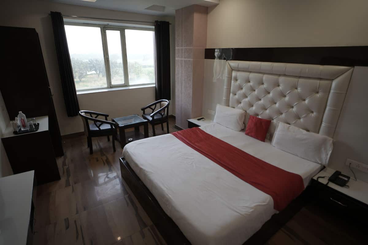 A hotel room with a large bed, a desk, two chairs, a window with curtains, and a view of the outdoors.