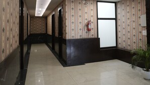 Un couloir d’hôtel avec un papier peint à motifs, un extincteur, une plante en pot et un luminaire au plafond.
