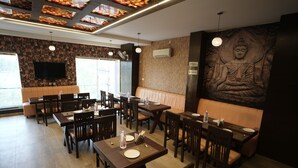 Un restaurant avec des tables et des chaises en bois, une grande statue de Bouddha accrochée au mur et un téléviseur à écran plat fixé au mur.