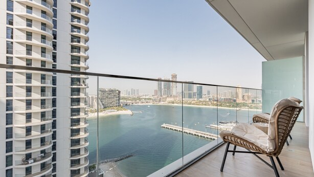 Un edificio alto con un balcón que da a un puerto deportivo y al horizonte de la ciudad.