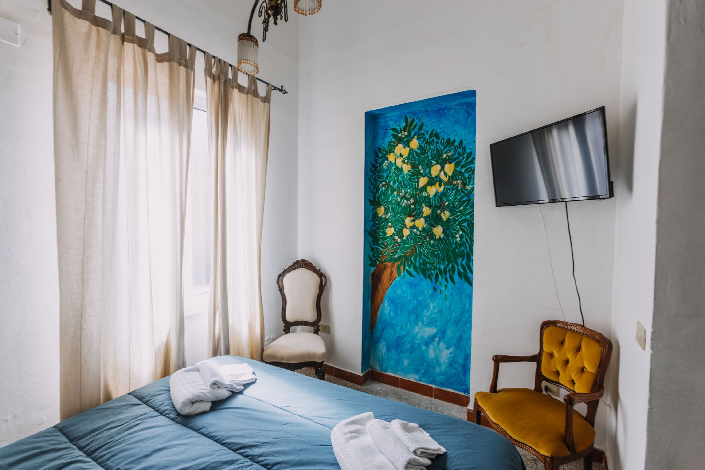 A bedroom with a bed, a chair, a painting, and a TV.