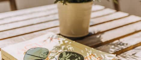 A book titled "Acqua Alta" with sunglasses on top, placed on a wooden table with a potted plant beside it.