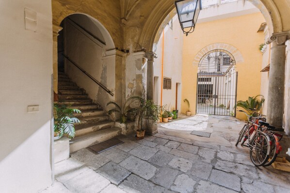 A narrow stone-paved courtyard with a staircase, potted plants, and a bicycle. - Real Umberto I by Wonderful Italy (Palermo)