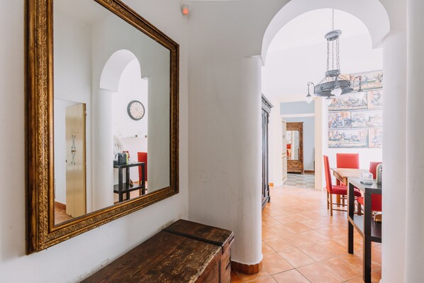 Um corredor com um espelho grande, um banco de madeira e uma sala de jantar com cadeiras vermelhas e uma mesa.