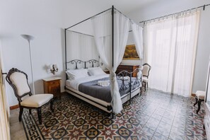 A bedroom with a four-poster bed, a chair, a nightstand, and a floor with patterned tiles. - Real Umberto I by Wonderful Italy (Palermo)