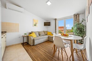 A modern living room with a sofa, dining table, and chairs. There is a flat-screen TV mounted on the wall, a potted plant, and a window with curtains. - Apartment Vito with Balcony (Galižana)