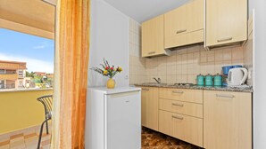 A compact kitchen with a refrigerator, wooden cabinets, and a window with a view of buildings.