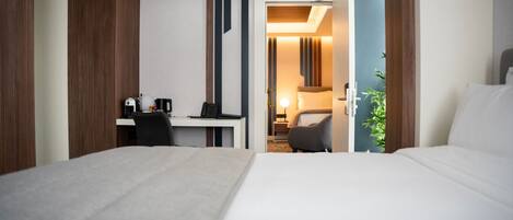 A hotel room with a bed, a desk with a chair, a lamp, and a plant.