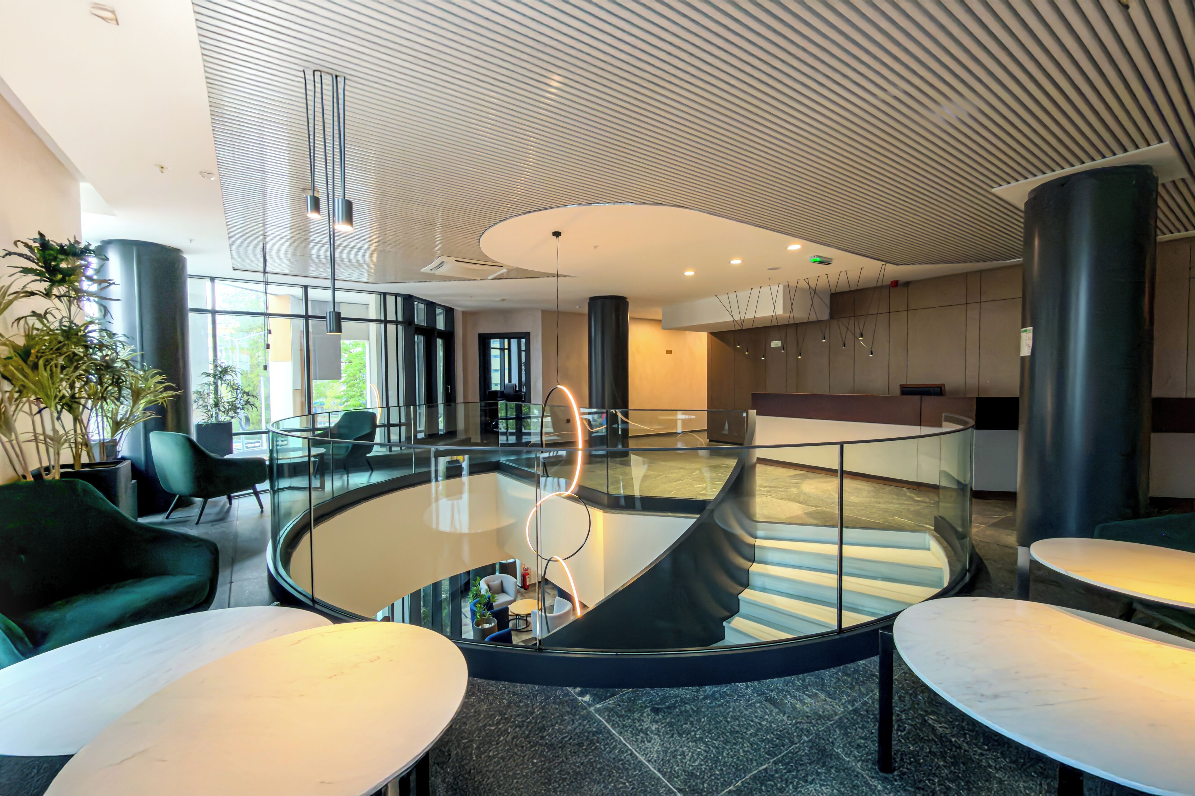 Un interior moderno con una zona de estar circular con piso de vidrio, una escalera en espiral y mobiliario contemporáneo.