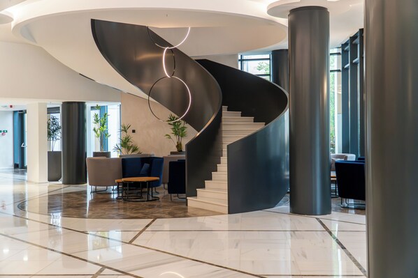 A modern lobby with a curved staircase, seating area, and large windows.