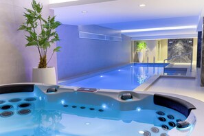 A modern indoor pool area with a hot tub, a potted plant, and a view of the outside.
