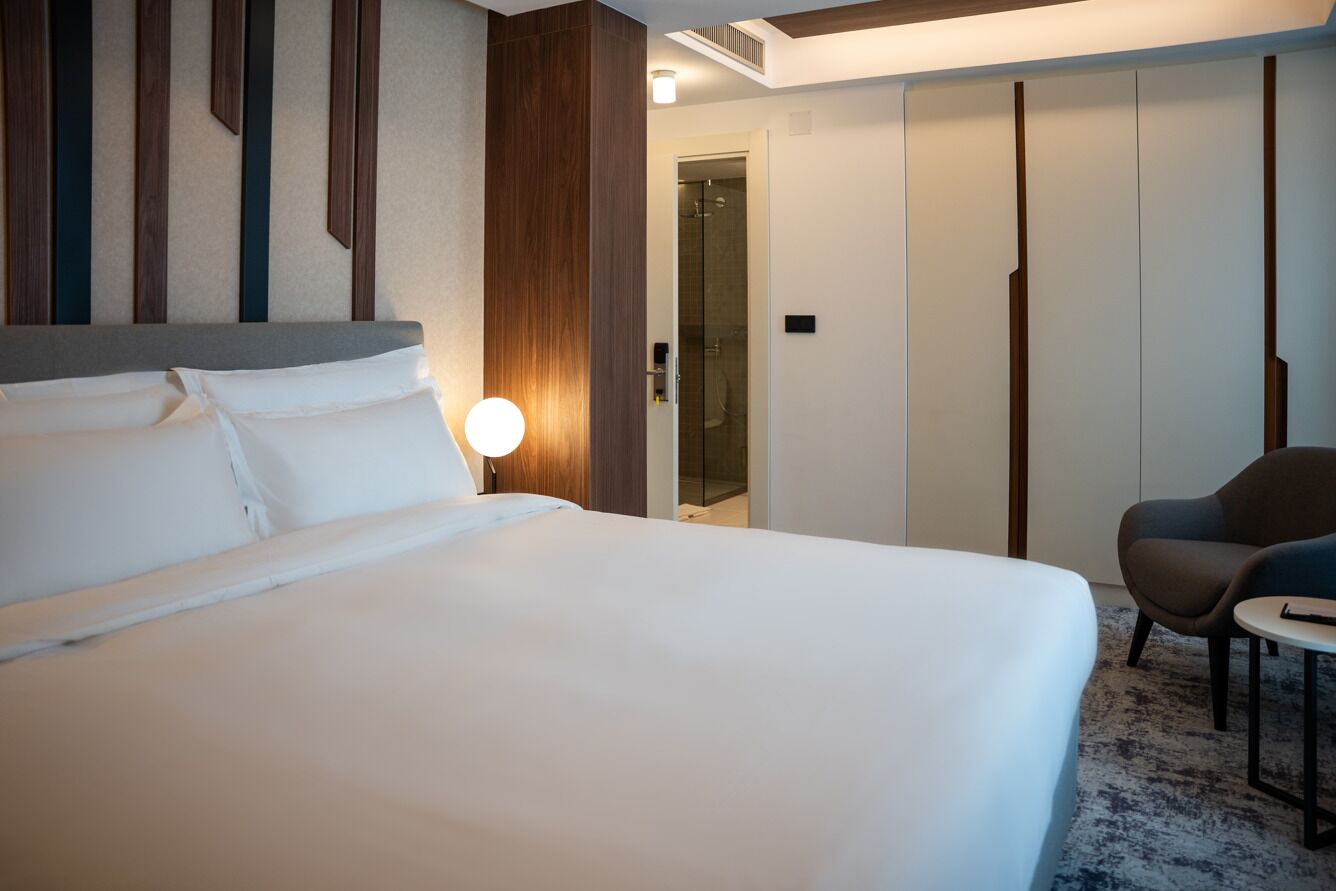 Una habitación de hotel con una cama grande, una lámpara de noche, una silla y una mesita.