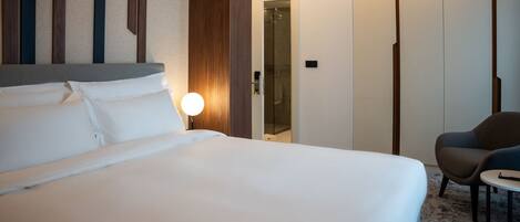 Una habitación de hotel con una cama grande, una lámpara de noche, una silla y una mesita.