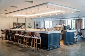 A modern bar area with a long counter, multiple stools, and a variety of bottles.