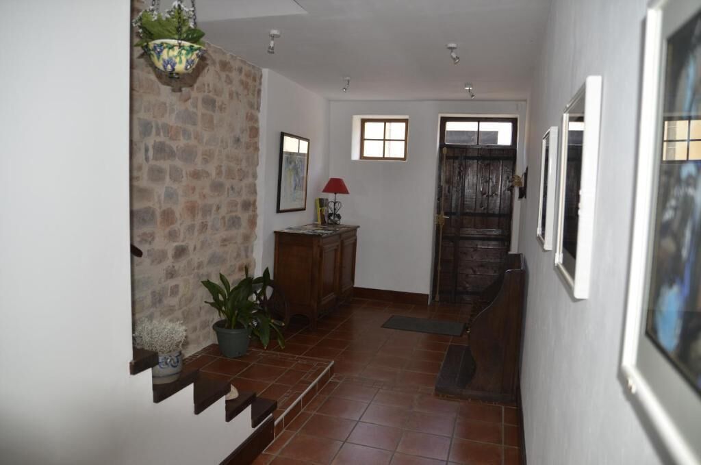 Un pasillo con pared de piedra, puerta de madera y una escalera que sube a otra habitación.